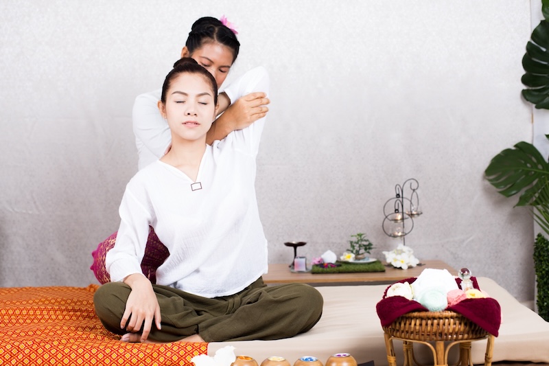 Frau genießt eine traditionelle Thai Yoga Massage bei Ariya Thai Massage in Augsburg, bei der eine Therapeutin ihren Arm und ihre Schulter dehnt.
